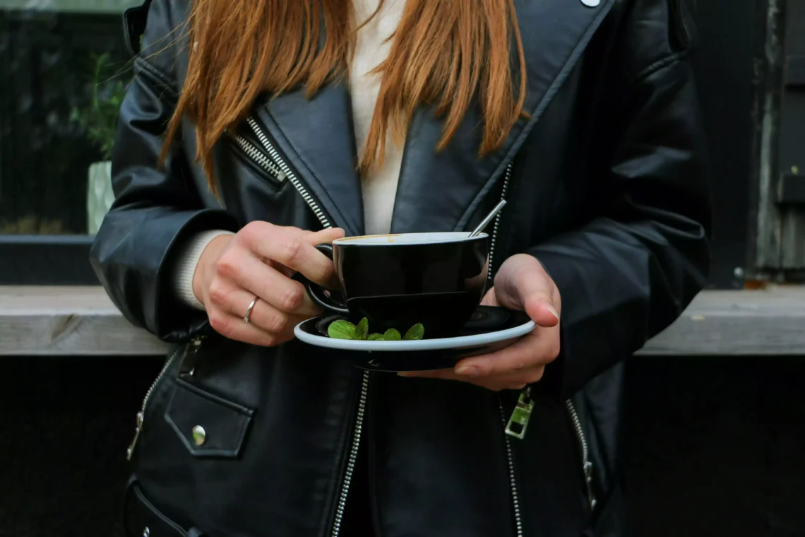 Raviver la couleur d'une veste en cuir. Femme portant un perfecto en cuir noir et tenant un café dans ses mains