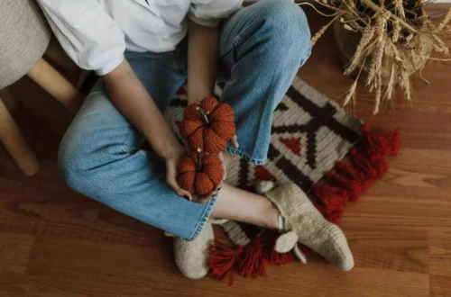 où acheter de la décoration d'automne ? personne assise en tailleur, tenant dans ses mains des citrouilles en tissu