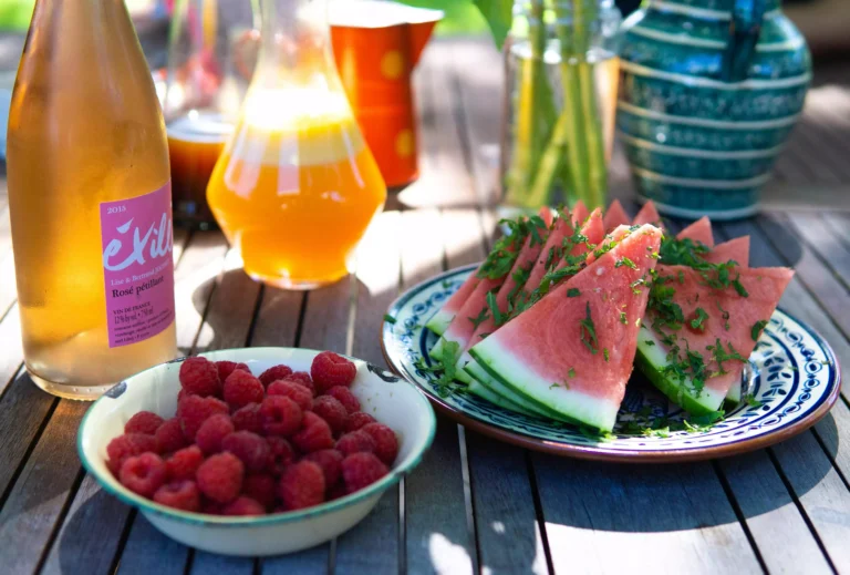 table d'extérieur, avec plats remplis de fruits (pastèque, framboises) et des carafes avec une bouteille de thé glacé