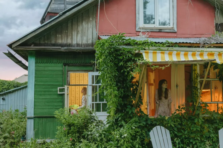 Maison en bois colorée, verte et rose, avec du lierre grimpant, et un store banne rayé jaune et blanc