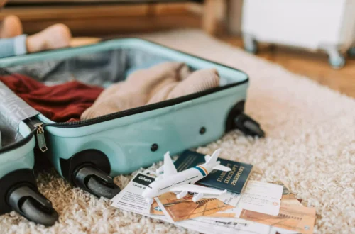 préparer sa valise pour le Japon, valise ouverte sur le sol avec des vêtements dedans et des papiers de voyage sur le sol et une figurine d'avion