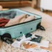 préparer sa valise pour le Japon, valise ouverte sur le sol avec des vêtements dedans et des papiers de voyage sur le sol et une figurine d'avion