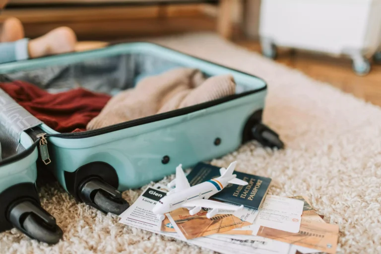 préparer sa valise pour le Japon, valise ouverte sur le sol avec des vêtements dedans et des papiers de voyage sur le sol et une figurine d'avion